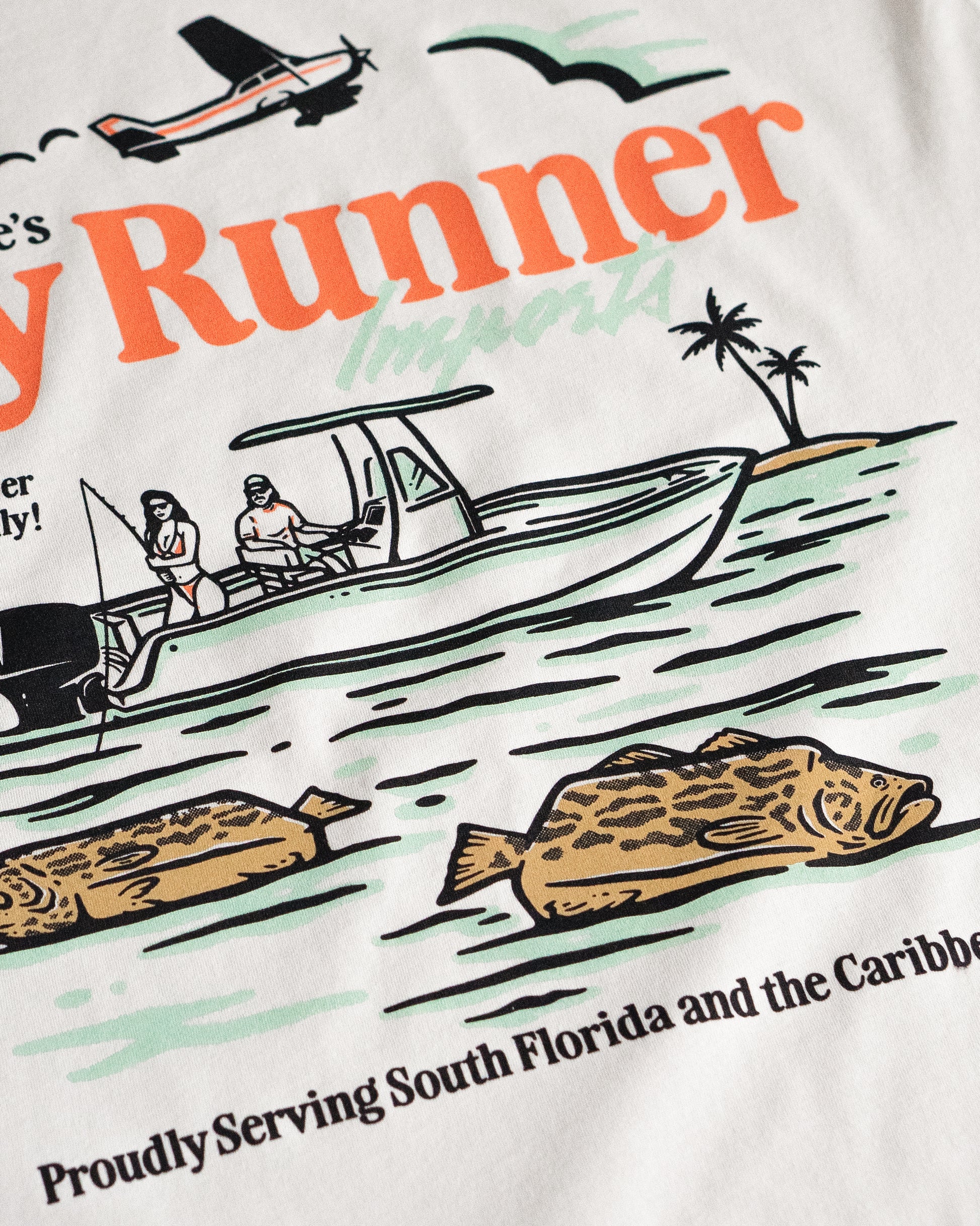Close-up of Jigalode Bay Runner Imports t-shirt print showing detailed artwork of a fishing boat, floating groupers, and flyover plane with tropical vibes