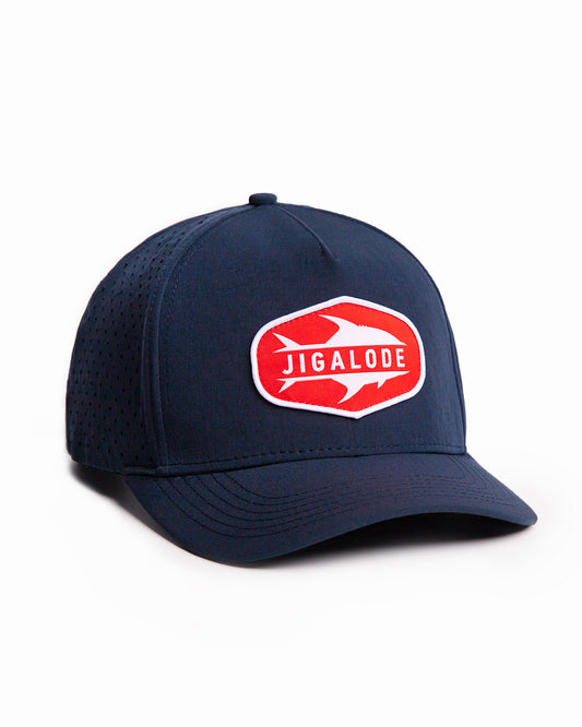 Angled shot of the Permit Performance Snapback. Navy blue hat with laser perforated holes and a red and white woven patch of a permit fish.