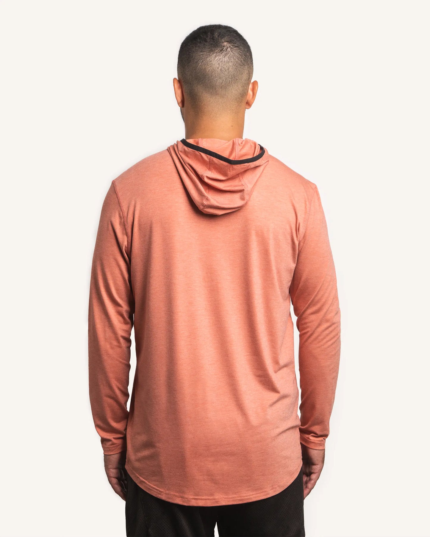 Back view of male model wearing the Jigalode Mighty Jig Performance Fishing Hoodie in rust orange with an all-over tropical plant pattern. The hoodie, with the hood on, provides UPF 30 sun protection and showcases its sleek design. The model demonstrates the hoodie's fit and style.