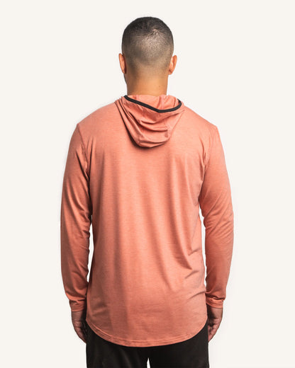 Back view of male model wearing the Jigalode Mighty Jig Performance Fishing Hoodie in rust orange with an all-over tropical plant pattern. The hoodie, with the hood on, provides UPF 30 sun protection and showcases its sleek design. The model demonstrates the hoodie's fit and style.