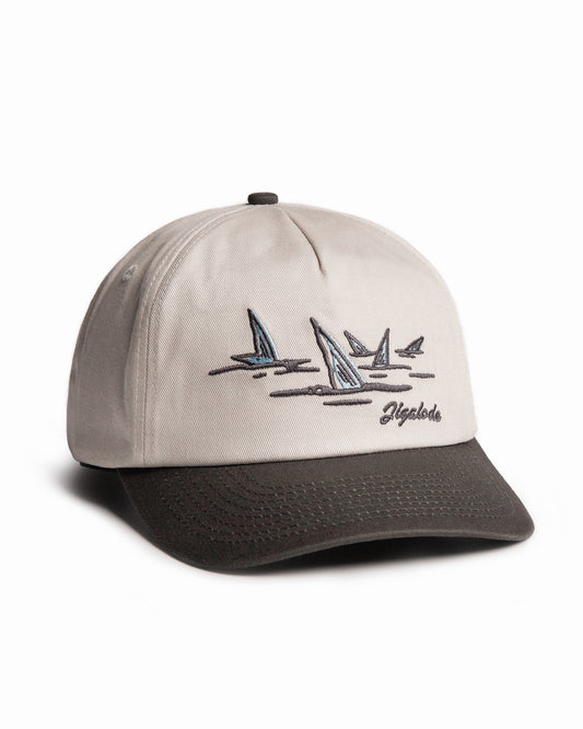 Angled shot of the Tailer Snapback. It is a tone toned hat (Natural crown with a dark gray brim) retro styled snapback with a school of bonefish tails embroidered in the front.