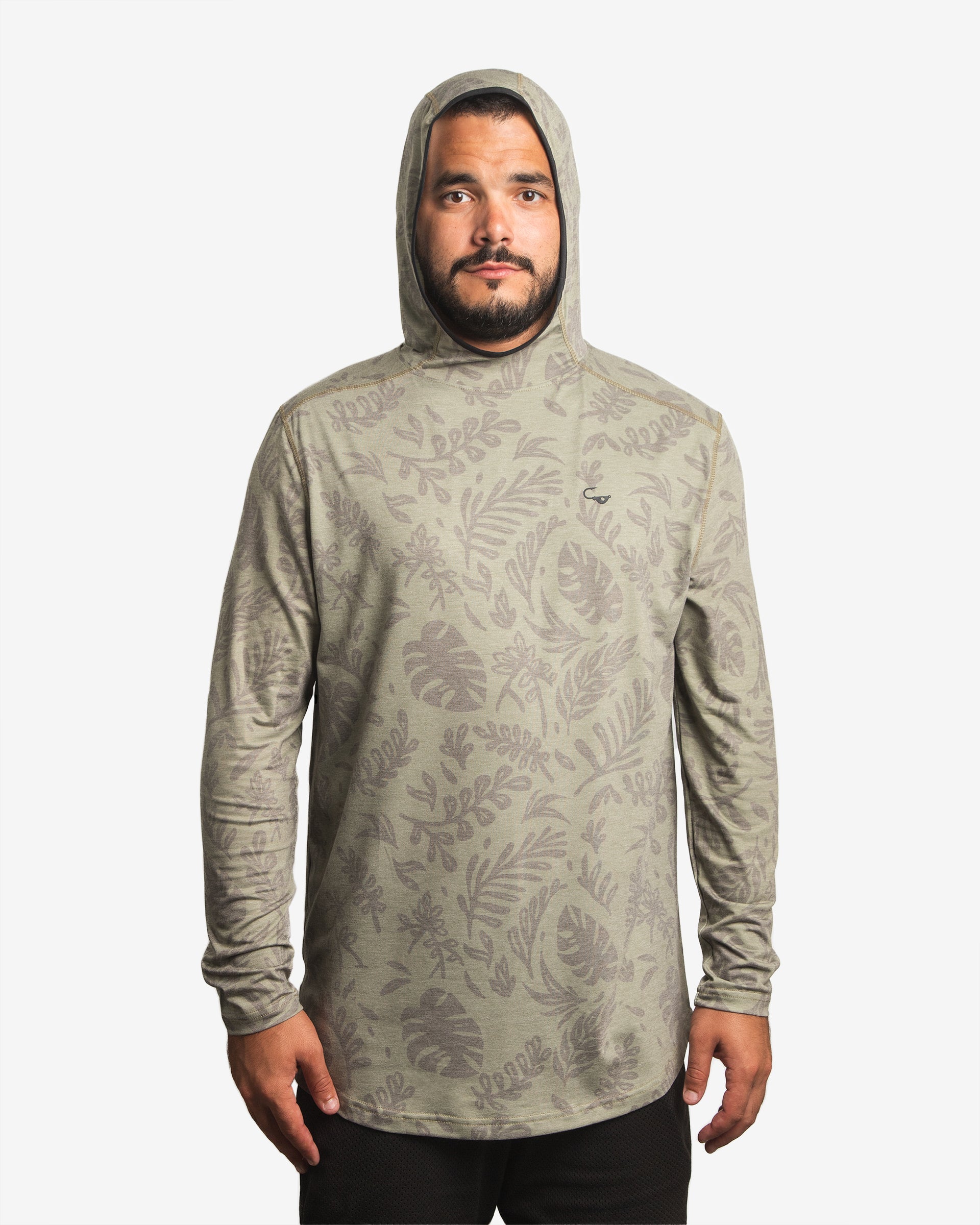 Front view of male model wearing the Jigalode Mighty Jig Performance Fishing Hoodie in moss green with an all-over tropical plant pattern. The hoodie, with the hood on, offers UPF 30 sun protection and features moisture-wicking properties. The model displays the hoodie's functionality and fashionable appeal.